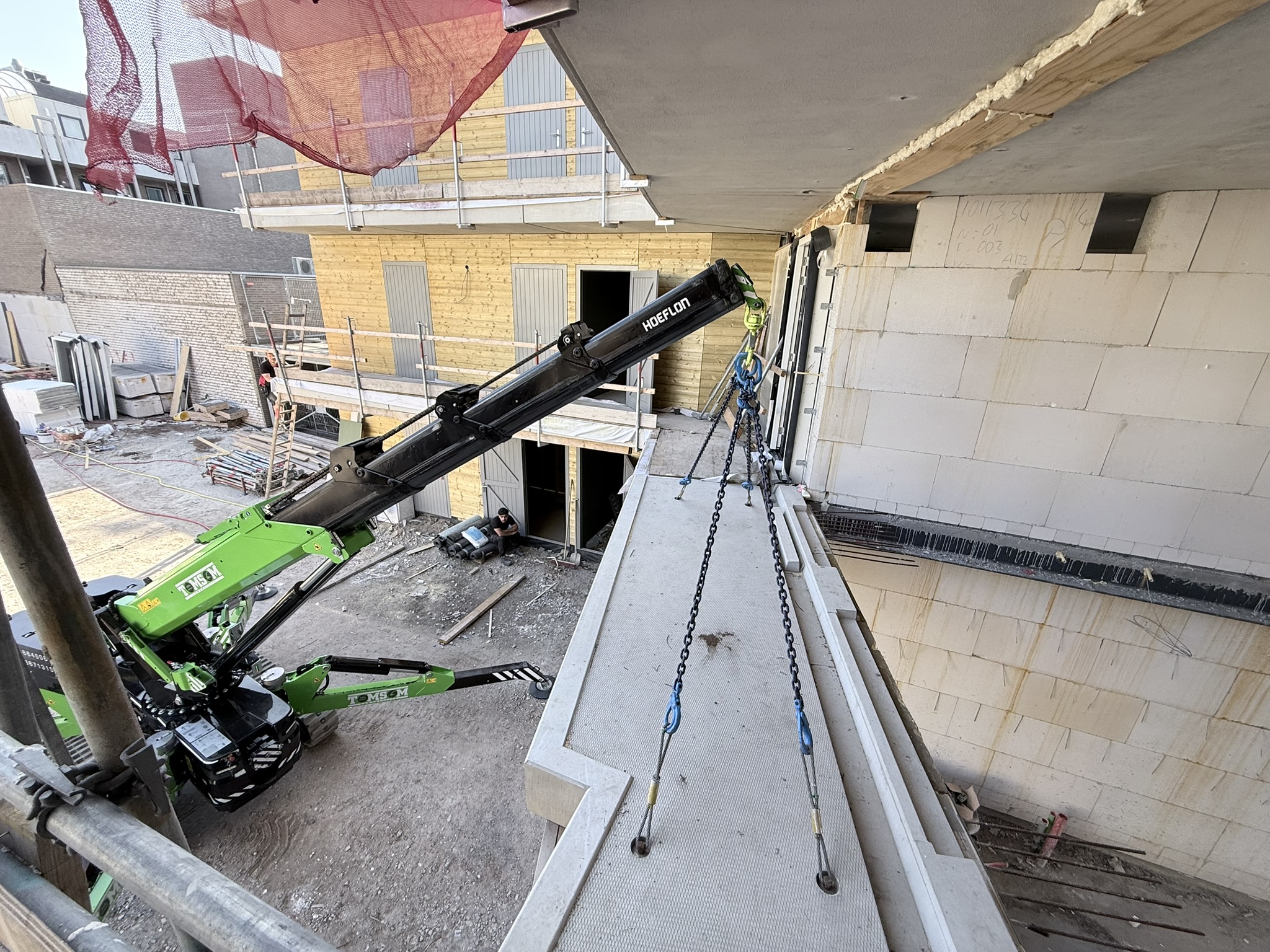 Betonen prefabvloer leggen in binnenhof woningcomplex met compacte hijskraan